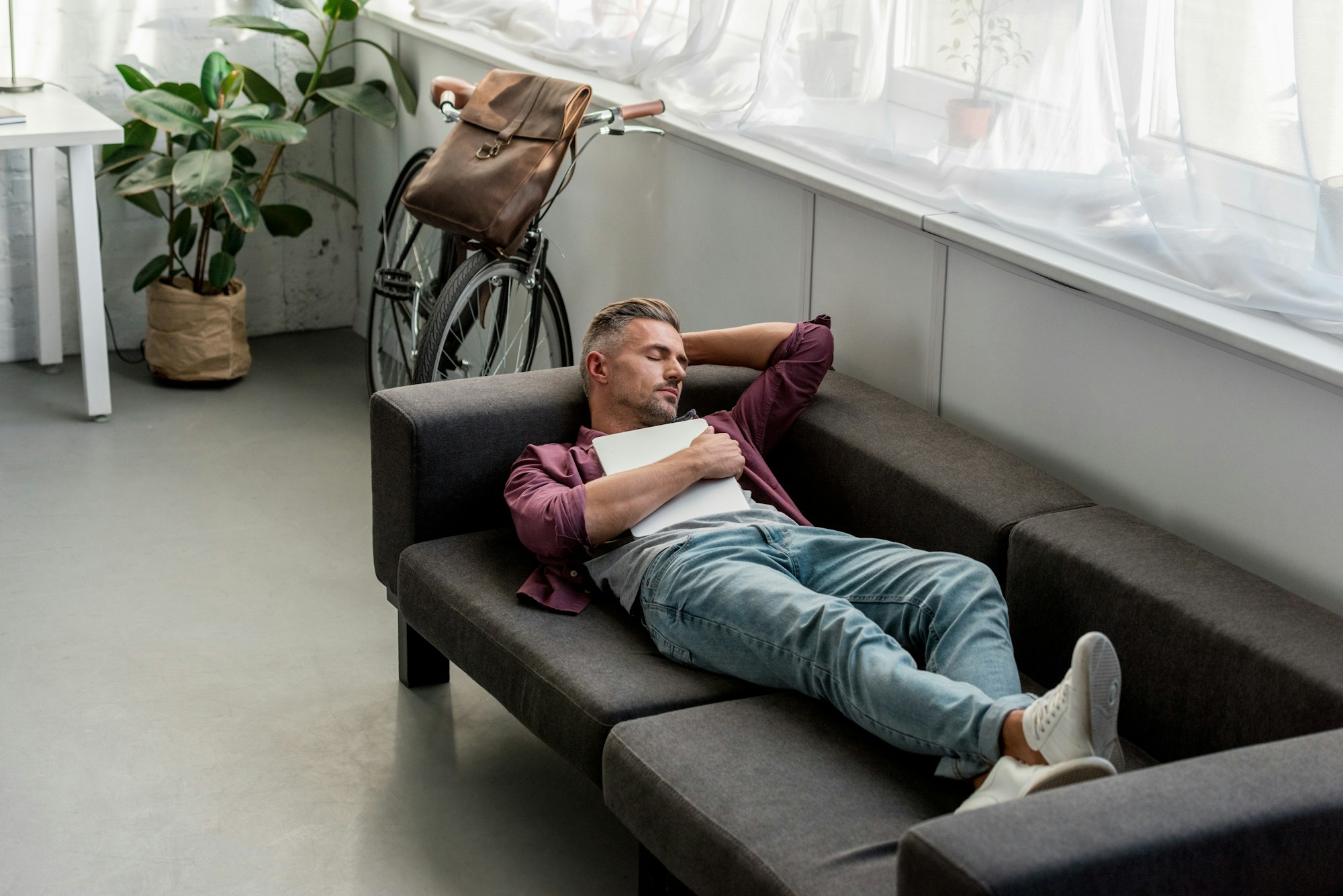 tired man laying on sofa with laptop and sleeping at home office