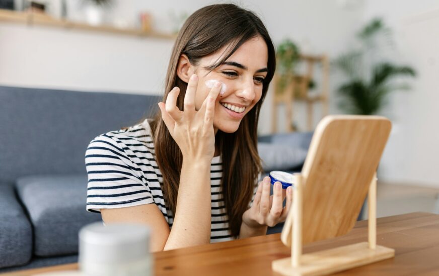 Smiling young pretty woman applying skin cream at her face